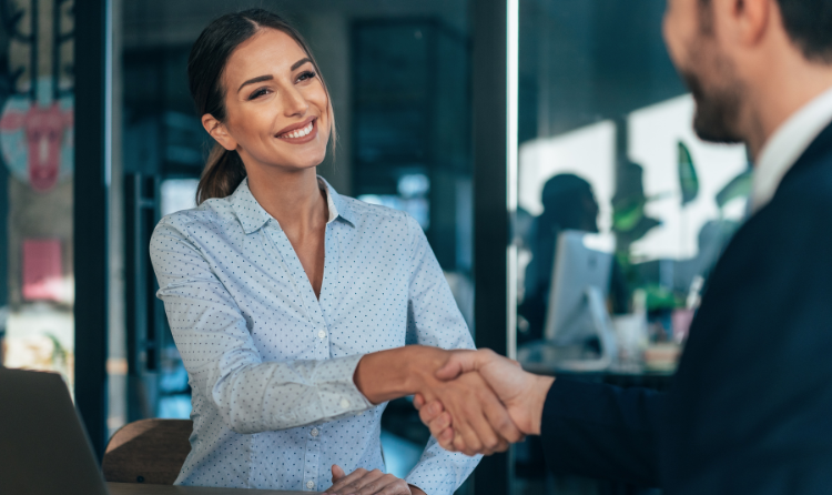A businesswoman is smiling while shaking hands with someone.